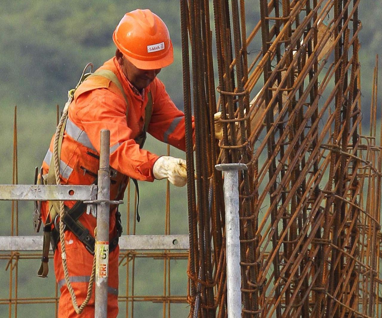 Trabajador de la construcción en un sitio de obras, vistiendo casco y uniforme naranja, manipulando varillas de acero para la estructura de un edificio.